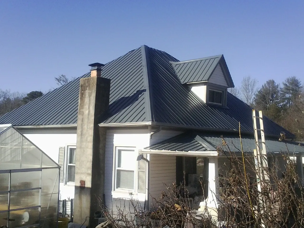 Dark blue standing seam metal roof on a white farmhouse with dormer — Slate & Tile Roof Repair by Roofing Brothers in Carlsbad