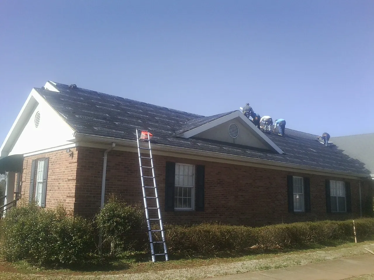 Crew tearing shingles off a brick ranch roof with a ladder set — Emergency Roof Repair work by our crew in Carlsbad