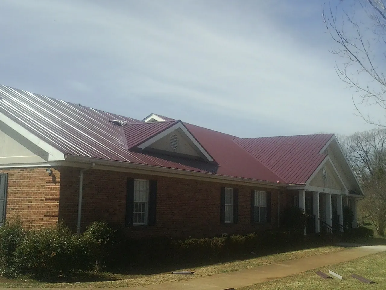 Red metal roof with gabled entries on a long brick building, from a Hail Damage Roof Repair job in Carlsbad