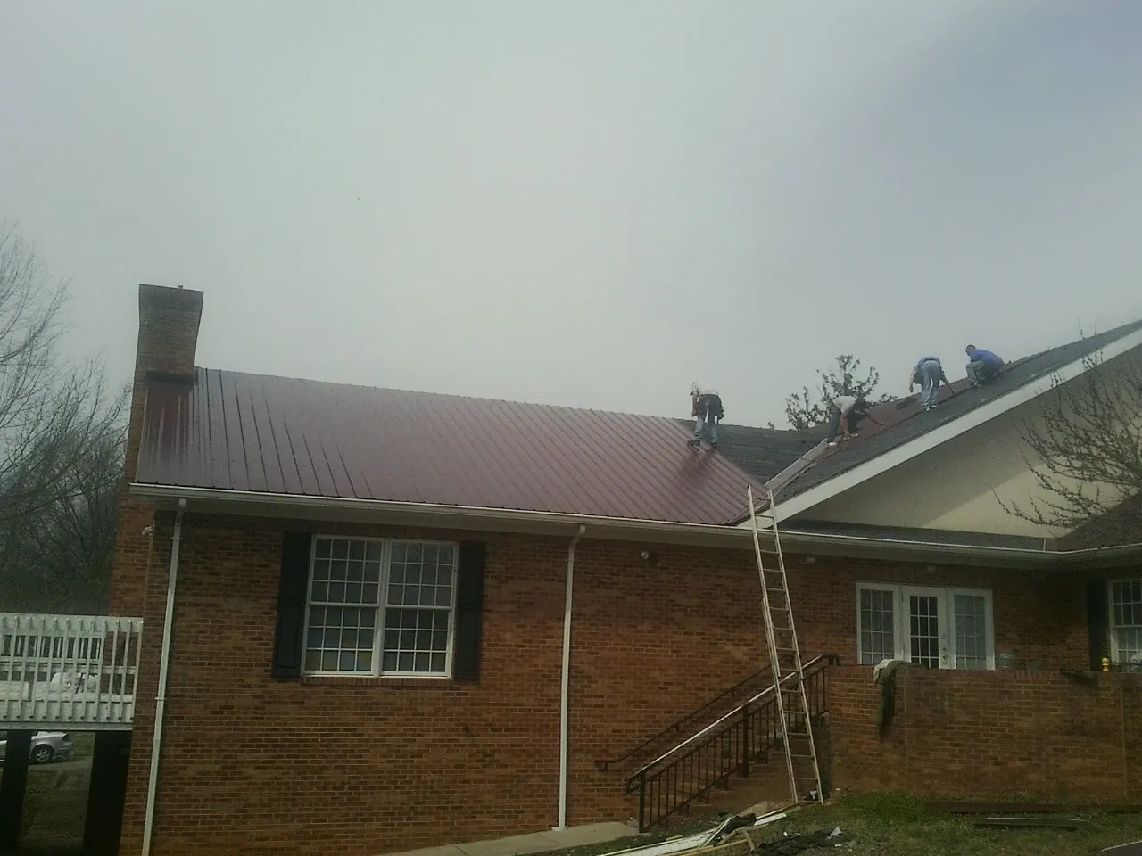 Crew setting red metal roofing panels on a brick home in Carlsbad