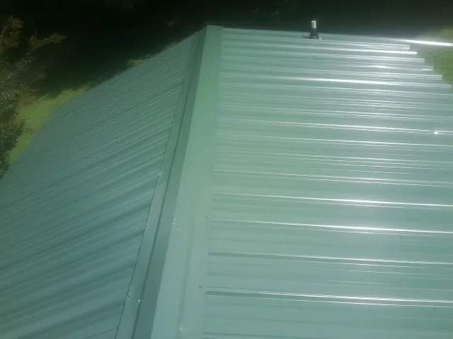New green metal panels meeting at the ridge of a roof — Flat Roof Repair work by our crew in Carlsbad