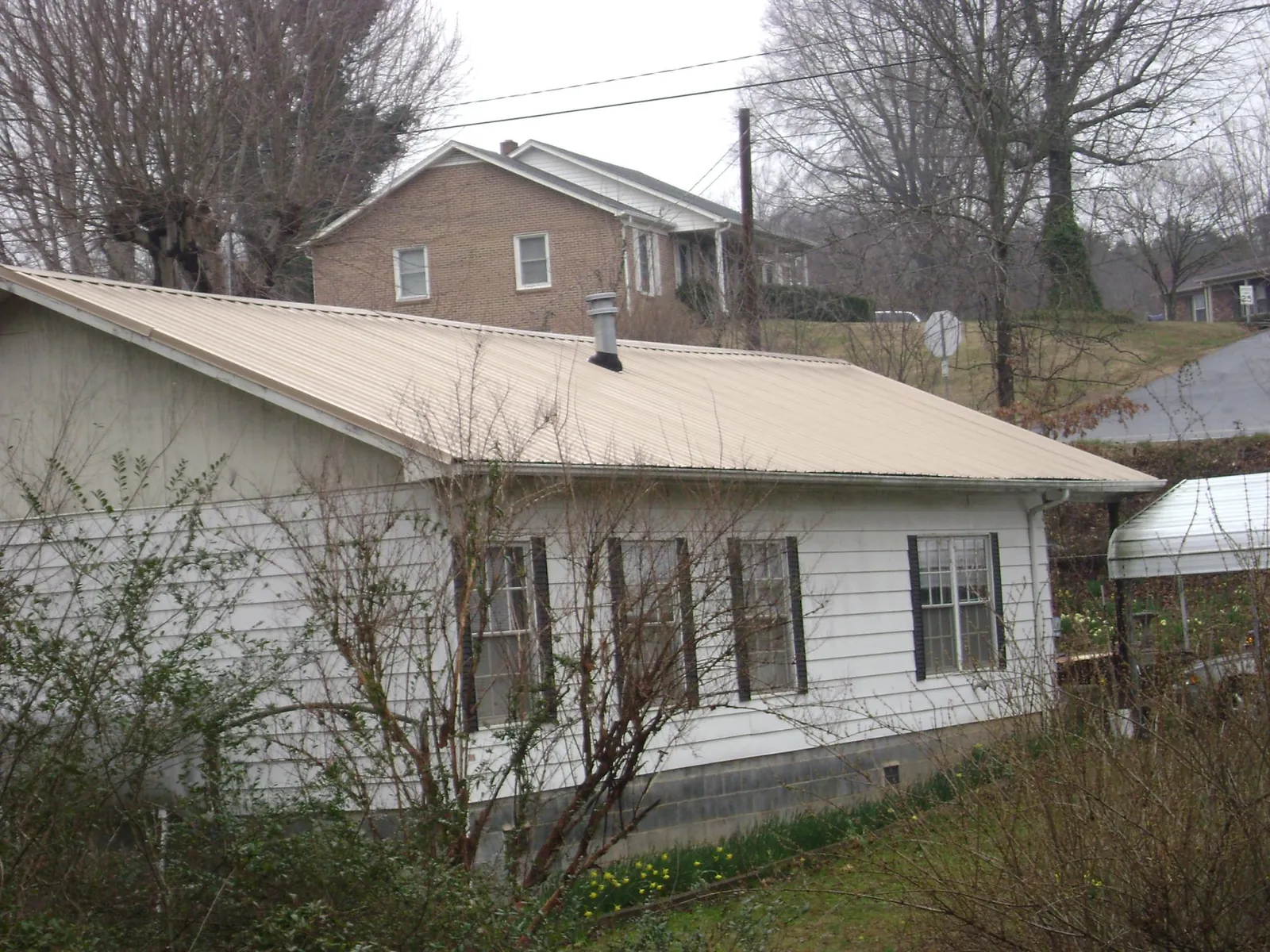 Tan metal roof on a white sided house set into a hillside — Commercial Roofing by Roofing Brothers in Carlsbad